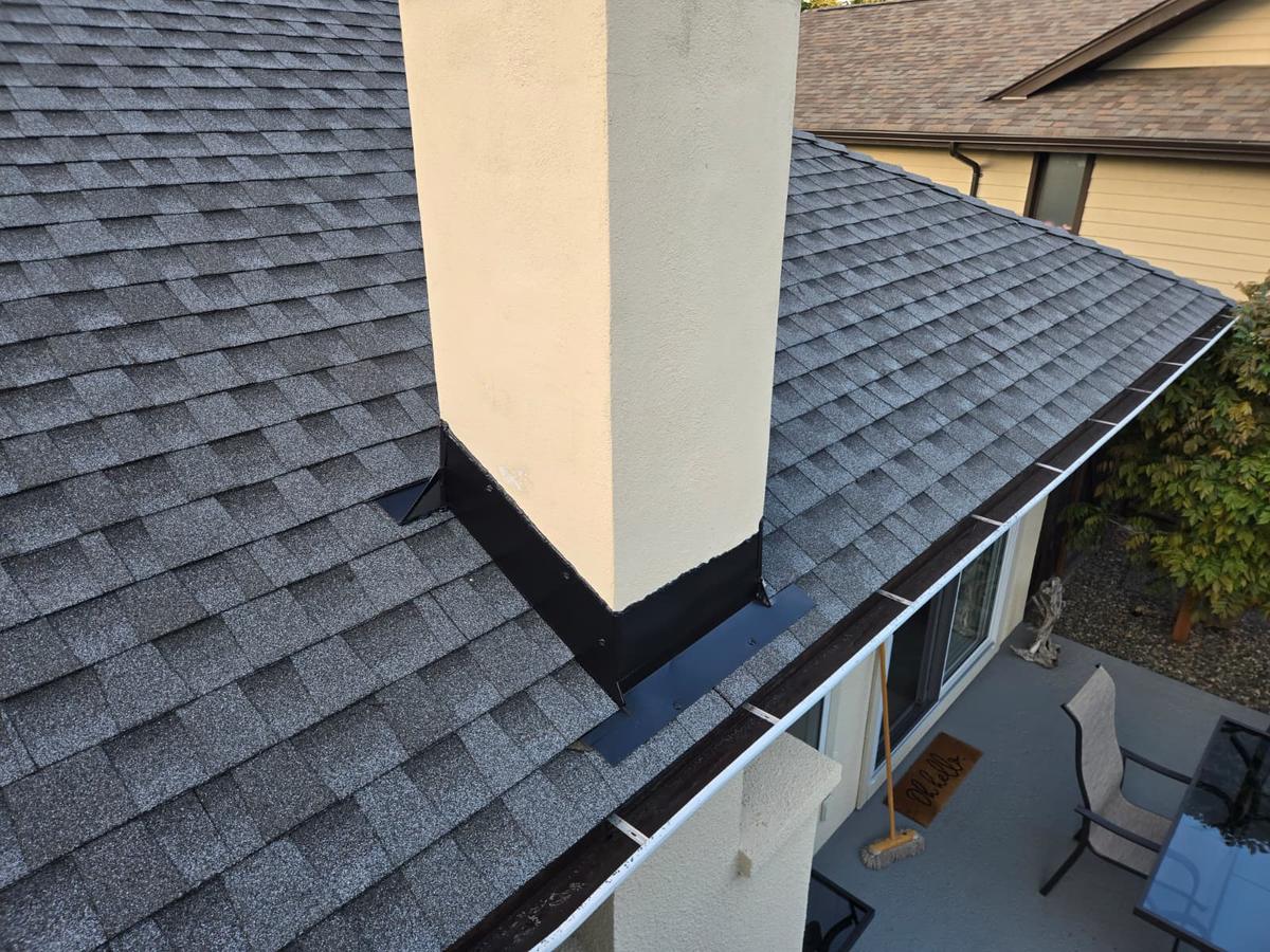 Chimney flashing and a gutter along the edge of a grey shingle roof