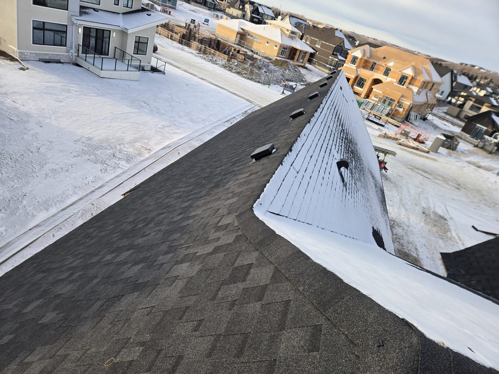Dark shingle roof with ridge vents in winter on a new home