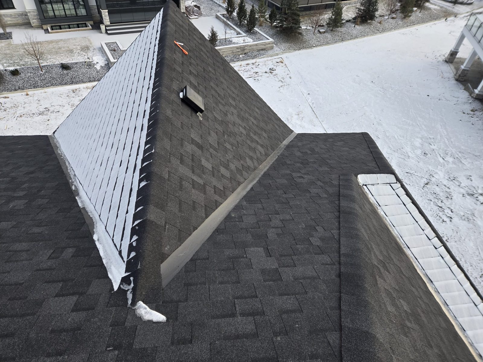 Dark shingle roof with a vent and flashing under fresh snow