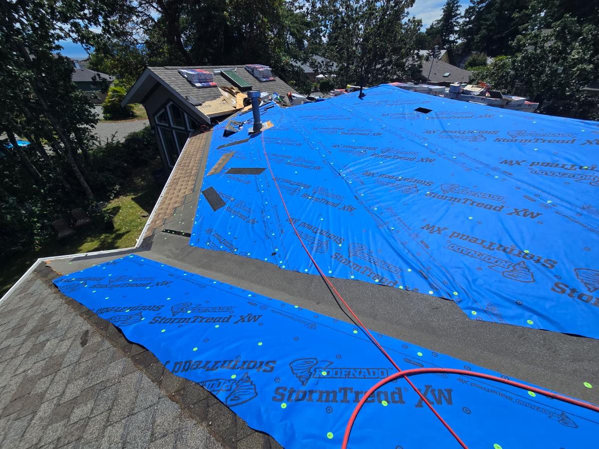Aerial view of a house with blue underlayment laid across the roof